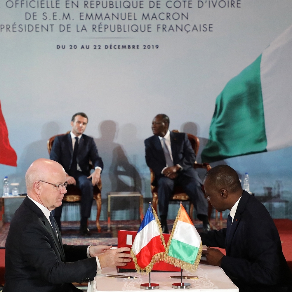 L'ex-PDG de Bouygues Construction Philippe Bonnave (à g.) et le ministre ivoirien des transports, Amadou Koné, signent le contrat du projet de métro d'Abidjan, en présence des présidents français et ivoirien Emmanuel Macron et Alassane Ouattara (en arrière-plan), à Abidjan, le décembre 2019.
