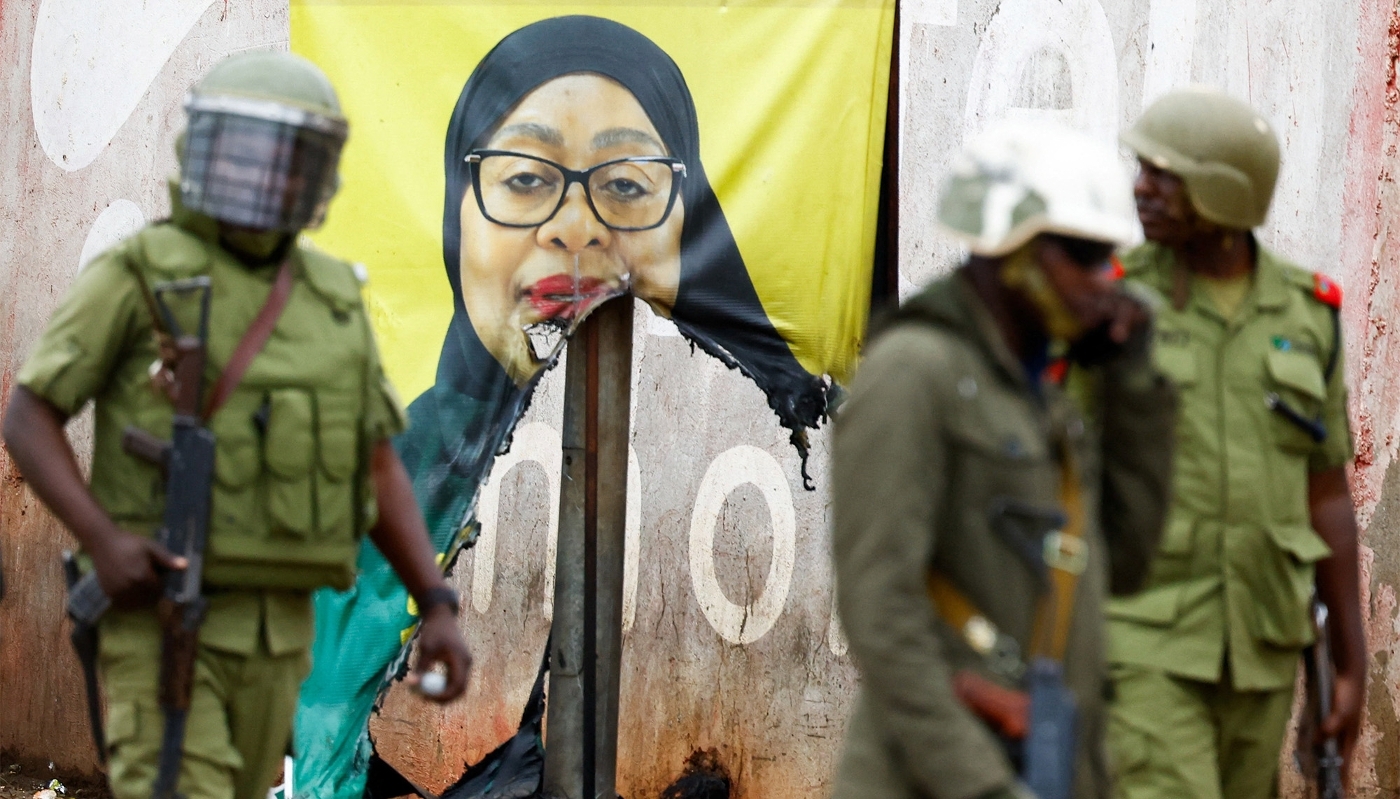 Des policiers antiémeutes passent devant une affiche électorale vandalisée de la présidente Samia Suluhu Hassan à Namanga, en Tanzanie, le 30 octobre 2025.