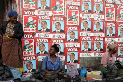 Des femmes vendent du charbon dans une rue de Maputo devant des affiches électorales du FRELIMO, le 31 août 2019.
