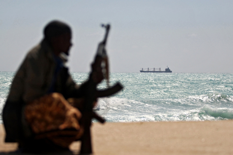 Un pirate somalien armé le long de la côte, le 7 janvier 2010. A l'arrière-plan, le cargo grec MV Filitsa est ancré au large de la ville de Hobyo, dans le nord-est de la Somalie, où il est retenu par des pirates.